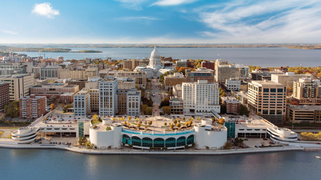 Aerial view of downtown Madison, Wisconsin, featuring the State Capitol building and Lake Monona under a bright sky.
