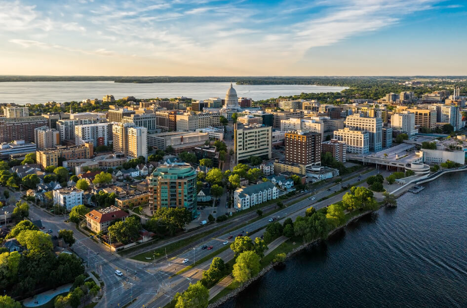 Aerial view of downtown Madison, Wisconsin, showcasing the State Capitol, surrounding buildings, and Lake Monona at sunset.