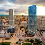 Downtown Milwaukee skyline at sunset, featuring tall modern buildings, busy streets, and a wide cityscape under dramatic clouds.