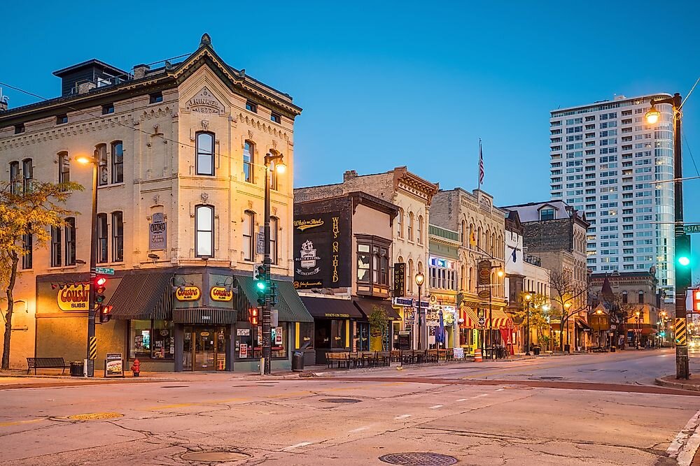 Historic downtown Milwaukee street at dusk with old brick buildings, shops, and city lights illuminating the scene
