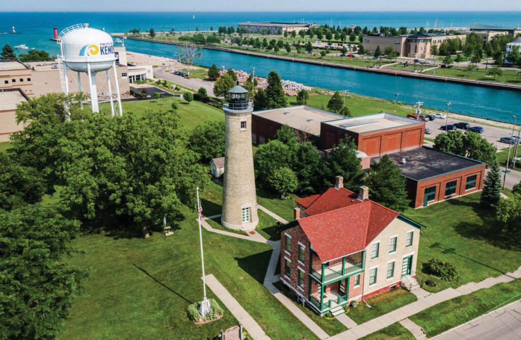 Aerial view of the Southport Lighthouse and historic buildings near the Kenosha harbor on a sunny day.