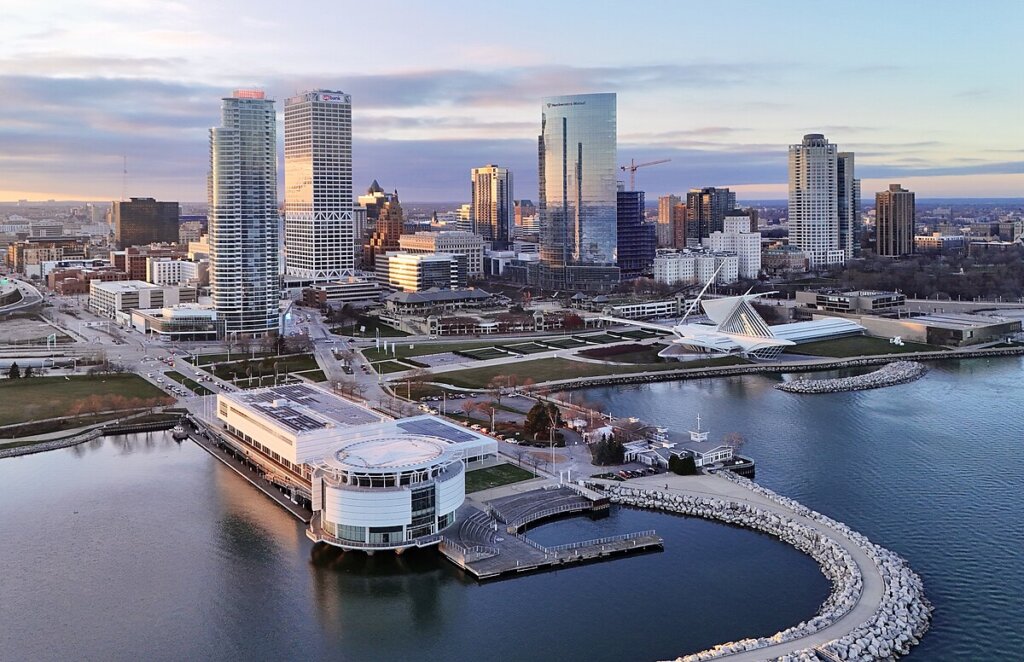 Aerial view of downtown Milwaukee with modern high-rise buildings, the Milwaukee Art Museum, and Lake Michigan shoreline at sunset.