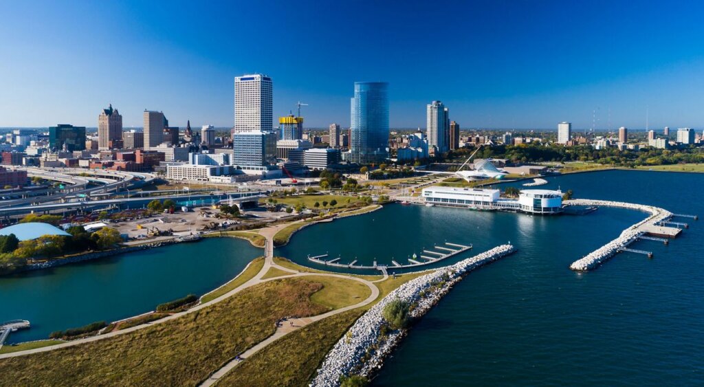 Aerial view of downtown Milwaukee featuring the lakefront, marina, and modern skyscrapers under a clear blue sky.