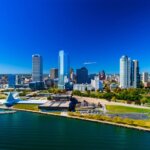 Aerial view of the Milwaukee skyline with tall buildings overlooking Lake Michigan on a clear, sunny day.