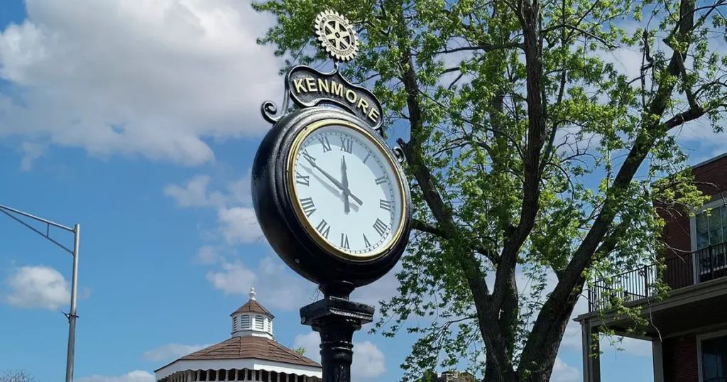 Decorative Kenmore village street clock with trees and blue sky in the background.