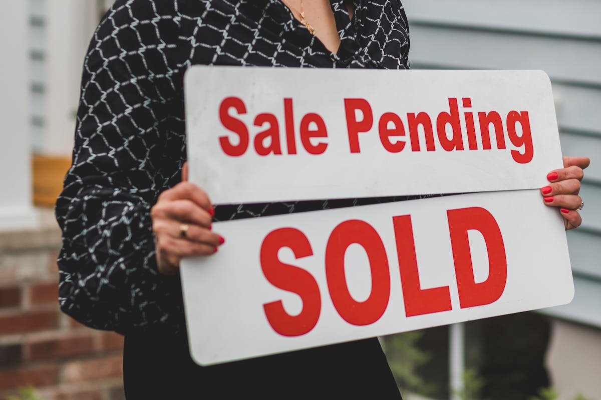 a person holding a sale pending sign in front of a house