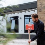 a man placing a for sale sign for buying a home into the ground in front of a building that is being sold