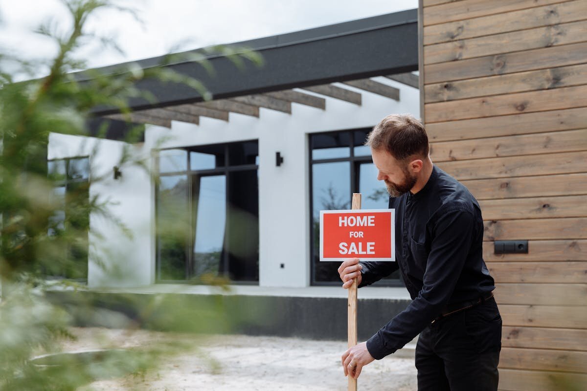 a man placing a for sale sign for buying a home into the ground in front of a building that is being sold