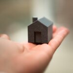 a person holding a small 3d printed house in their palm