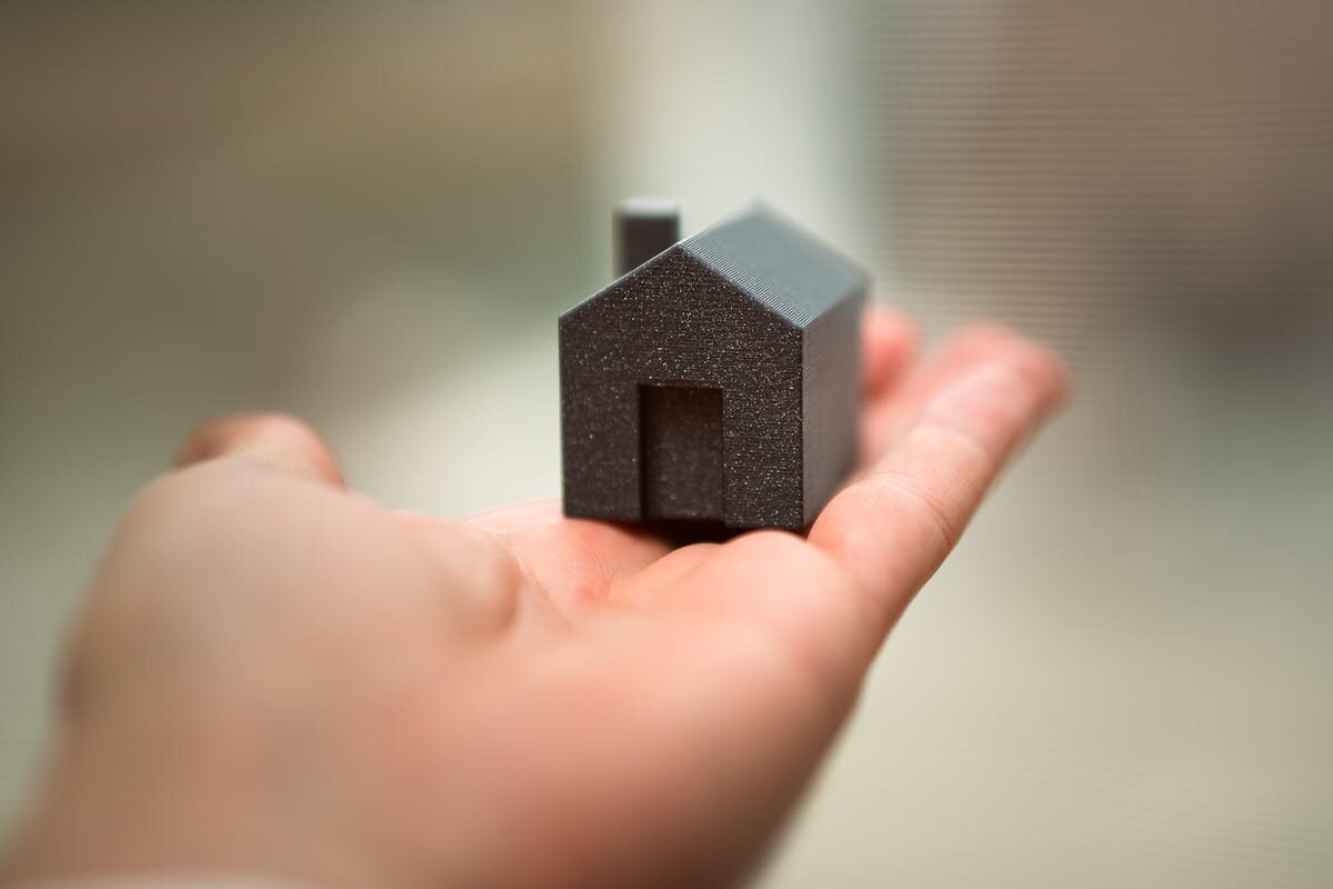 a person holding a small 3d printed house in their palm