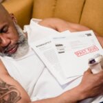 A man who is asleep on the couch with a past due notice on his chest