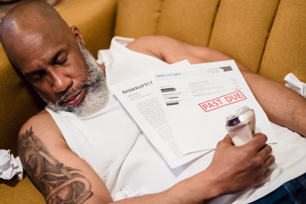 A man who is asleep on the couch with a past due notice on his chest