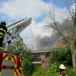 A house that is on fire and a firetruck spraying water on it