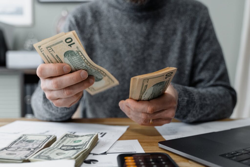 A person counting money on a table with a laptop next to them