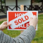 A person putting a sold sticker over a house for sale sign