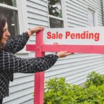 A lady putting a sale pending sign in front of a house