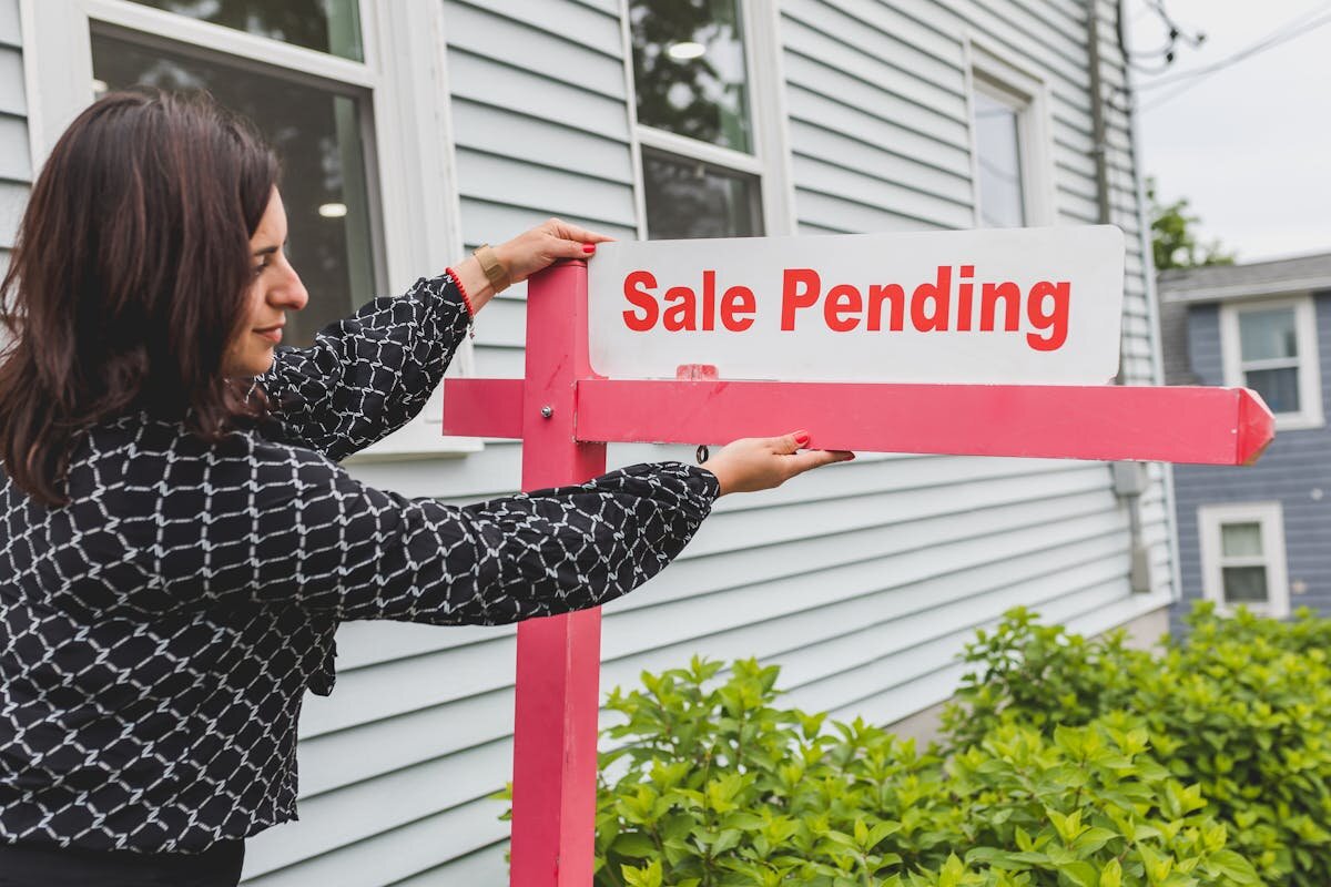 A lady putting a sale pending sign in front of a house