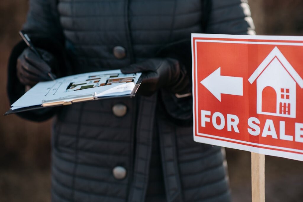 A person writing on some paper in front of a for sale sign