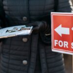 A person writing on some paper in front of a for sale sign