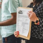 A person holding a house listing on a clipboard in front of them