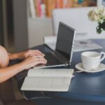 A person sitting on their laptop with a cup of coffee next to them