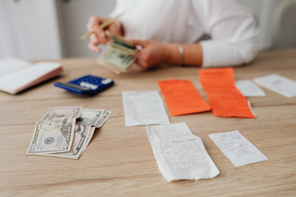 A person counting money on a table with some receipts next to them