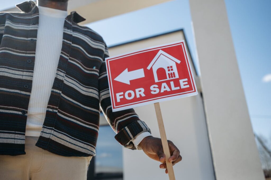 A person placing down a for sale sign on the lawn of a home