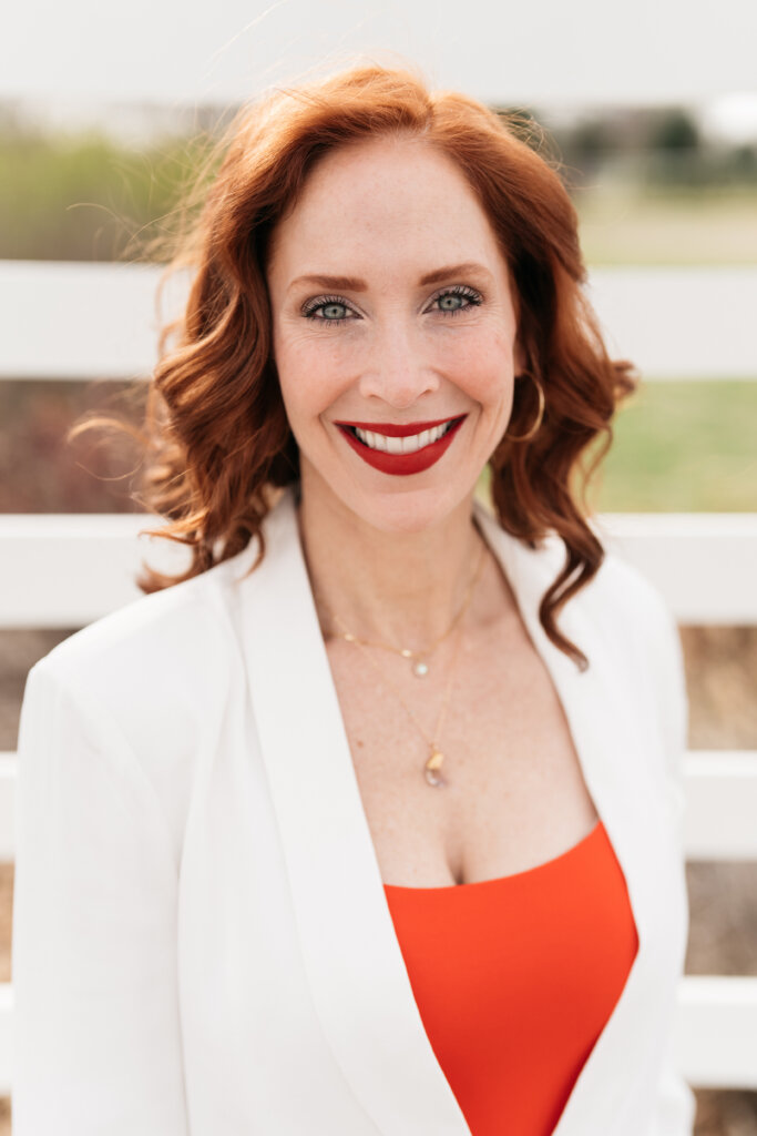 Jonesie with long red hair in a red shirt and white blazer