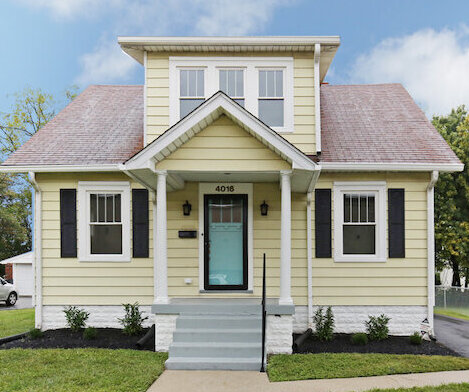 Yellow 1 1/2 story yellow bungalow with Black Shutters with covered gray front porch.