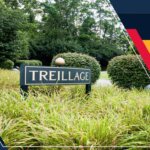 A sign that says trelliage in front of bushes and trees.