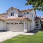 A home with two garages and a grassy yard that is protected from stuff that endangers the roof.