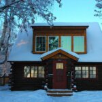 A small log cabin covered in snow, requiring immediate removal to ensure a safe roof.