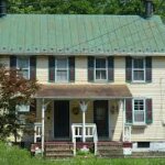 A yellow house with a green roof perfectly blends in the middle of a field, requiring occasional residential roofing maintenance.