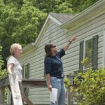 Two women make your roof ready for summers by standing on a ladder in front of a house.