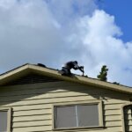 A local roofing contractor is standing on the roof of a house.