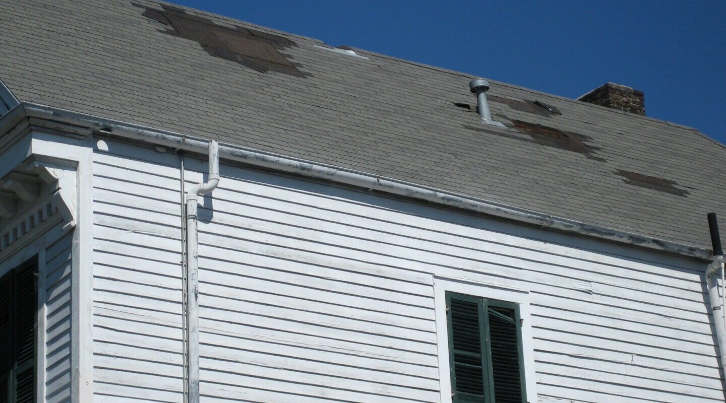 A white building that has wind damage causing a leaking roof.