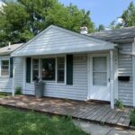 A small white house with a front porch in need of a roof inspection.