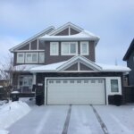 An energy-efficient house in the snow with a garage and driveway.