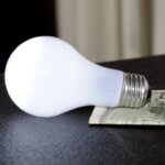 An energy efficient light bulb sitting on top of a dollar bill.