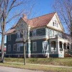 A house with a distinguished copper roofing, located on the corner of a street.