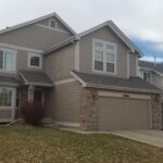 A house with mold and algae growing on its exterior walls and a garage in front of it.