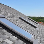 A shingled roof with two leaky skylights on it.