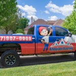 A blue and white truck parked in front of a house undergoing siding replacement.