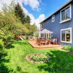 A backyard with a blue house and green grass, requiring siding replacement.