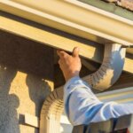 A man is diligently working on the gutters of a house, ensuring there is no gutter clogging.