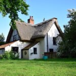 A house with a thatched roof in the middle of a field, adorned with charming moss growth.