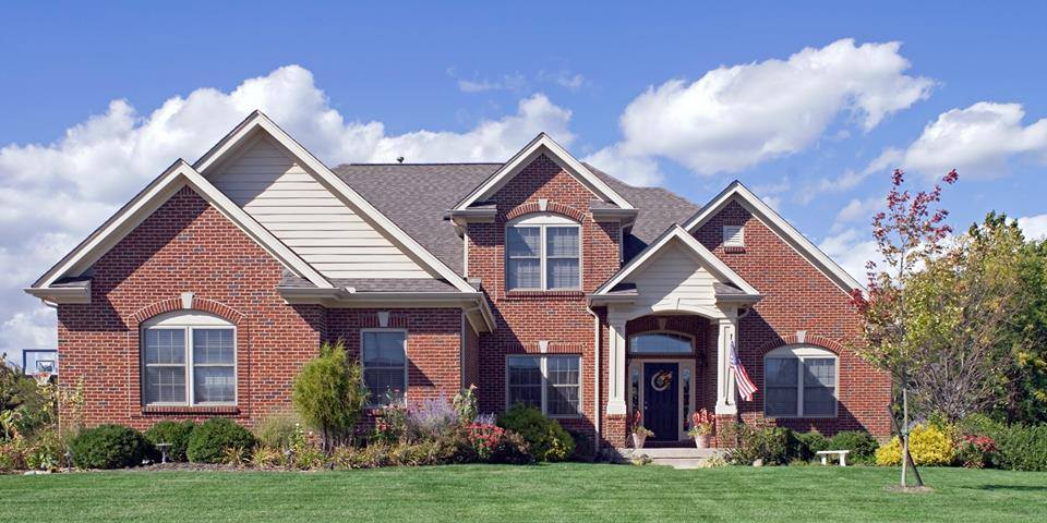 A brick home with a green lawn in need of roof replacement.