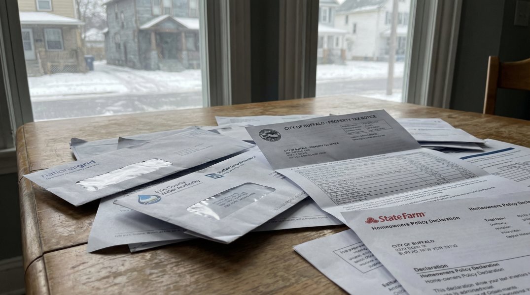 Property tax notice, utility bills and insurance statements on a kitchen table — the true carrying cost of a Buffalo NY home