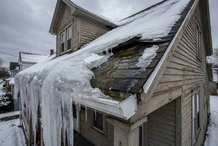 Ice dam with water backing up under shingles at roof eave — pre-1970 Buffalo NY home, peak damage season December through February