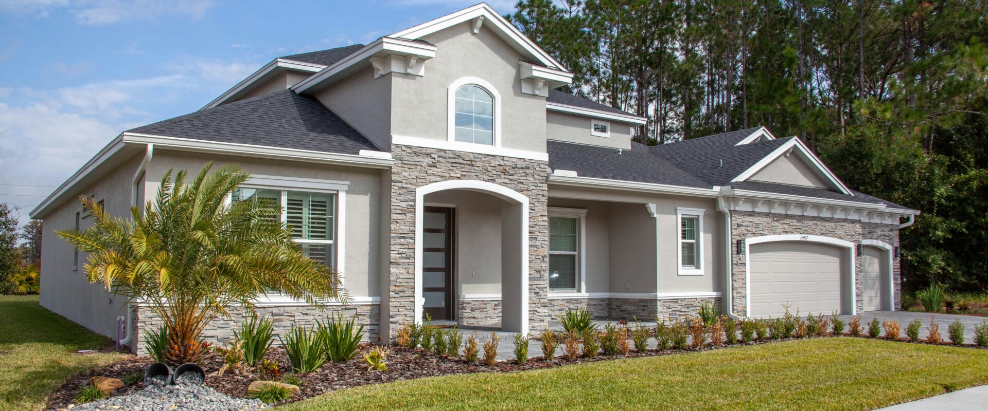 modern suburban home with stone accents, manicured lawn, and three-car garage